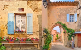 Picture of the Grignan village, with window and arch made of golden stones, with pots of colourful flowers.