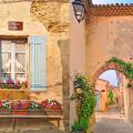 Picture of the Grignan village, with window and arch made of golden stones, with pots of colourful flowers.